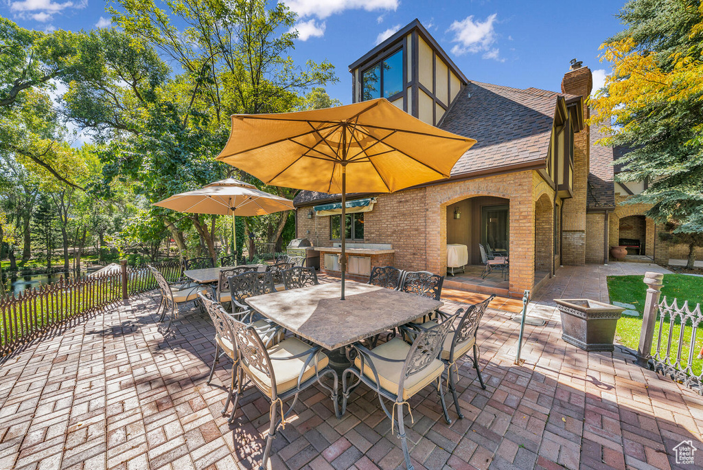 View of patio with fence, outdoor dining space, a fireplace, and grilling area