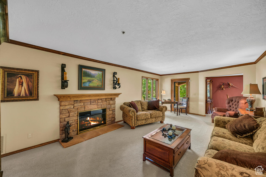 Carpeted living room featuring crown molding, a stone fireplace, baseboards, and a textured ceiling