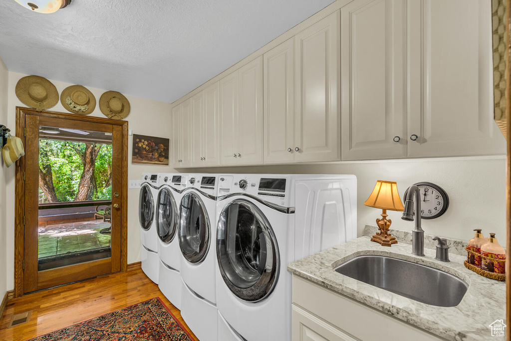 Laundry room with independent washer and dryer, cabinet space, light wood finished floors, and a textured ceiling
