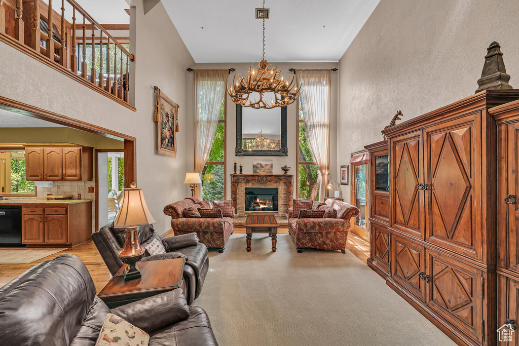 Living area with a chandelier, a high ceiling, healthy amount of natural light, a lit fireplace, and light carpet