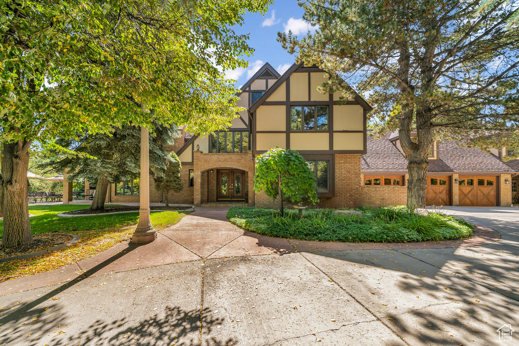 Tudor house featuring brick siding, an attached garage, driveway, and french doors