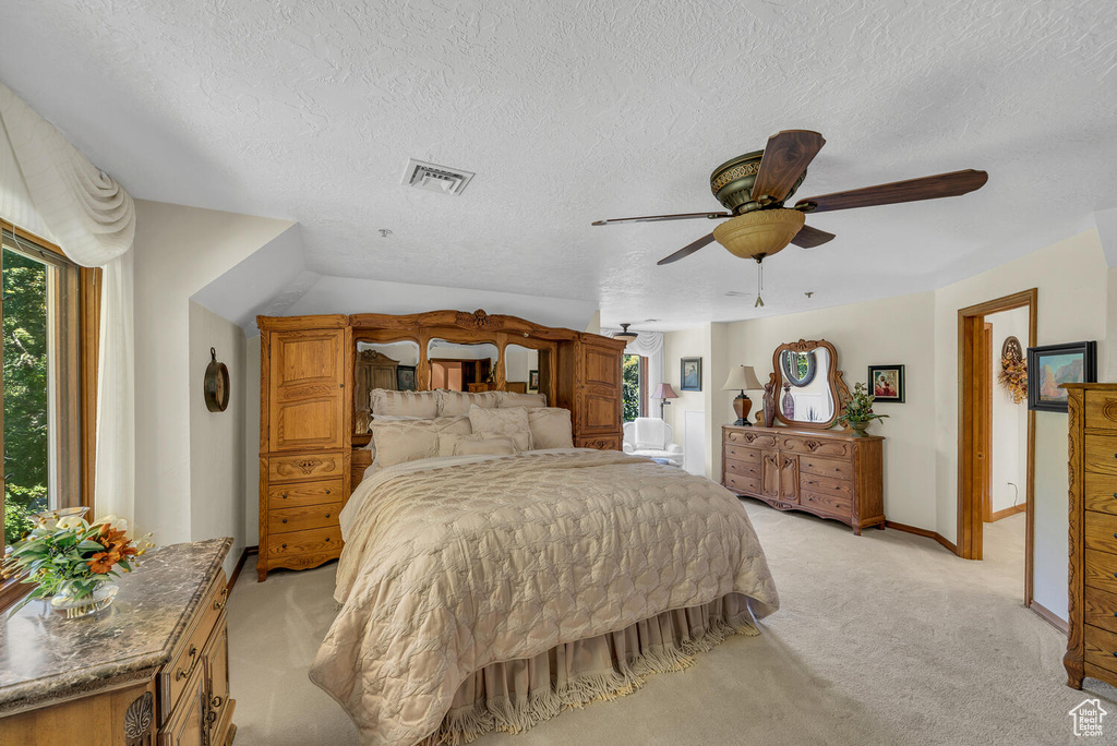 Bedroom with light colored carpet, multiple windows, a textured ceiling, ceiling fan, and baseboards