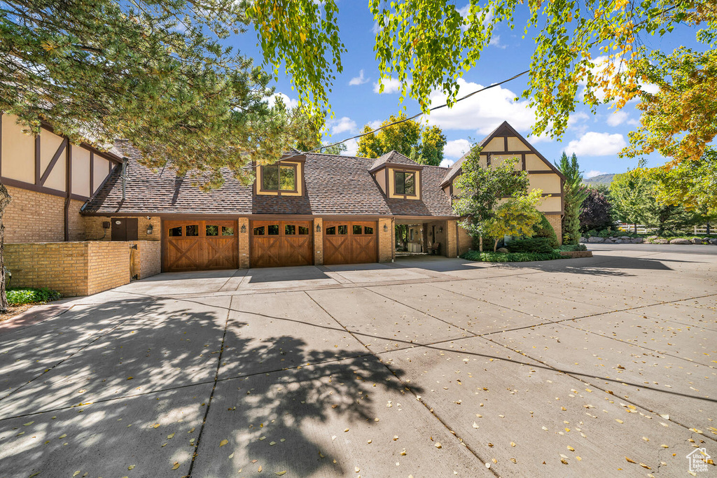 Tudor home with brick siding, driveway, a garage, and roof with shingles