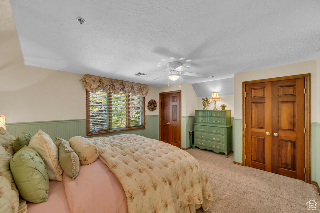 Carpeted bedroom with wainscoting, a textured ceiling, and a ceiling fan