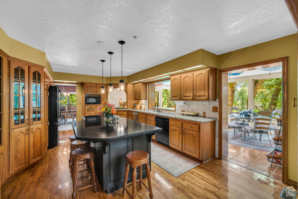 Kitchen featuring black appliances, a sink, a textured ceiling, a breakfast bar, and healthy amount of natural light
