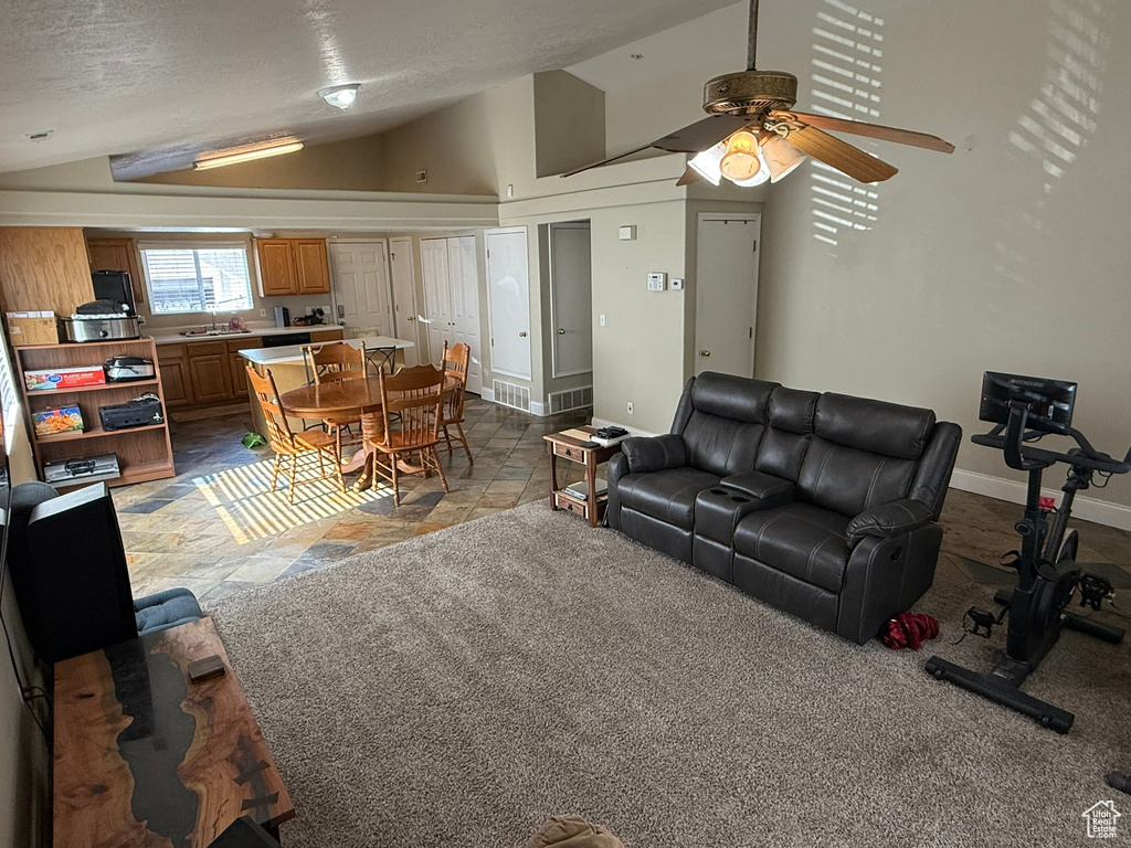 Living area with lofted ceiling, a ceiling fan, baseboards, and light stone finish floors