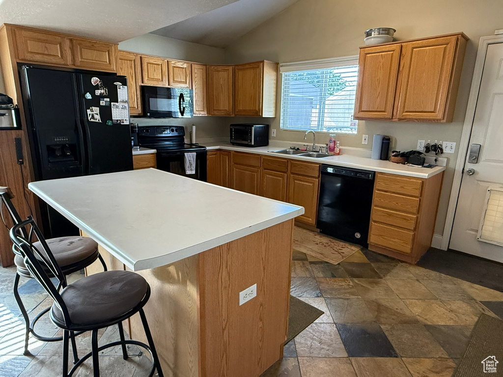 Kitchen featuring black appliances, a sink, a kitchen breakfast bar, vaulted ceiling, and stone finish flooring