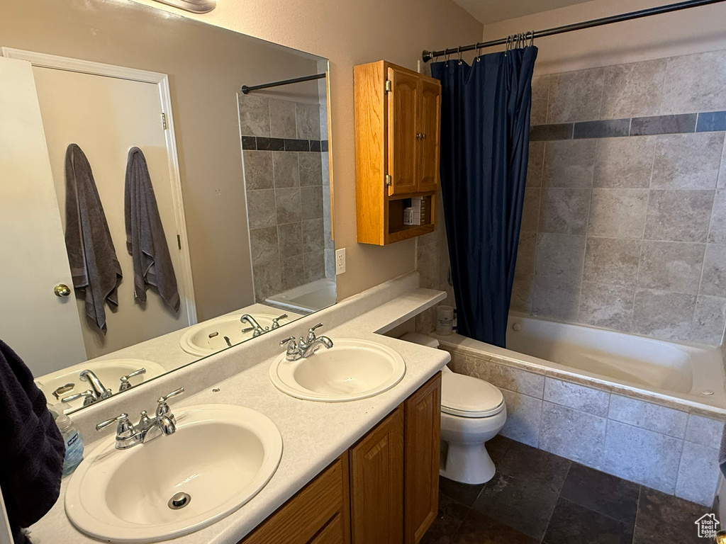 Bathroom with tiled shower / bath, stone finish floors, double vanity, and toilet