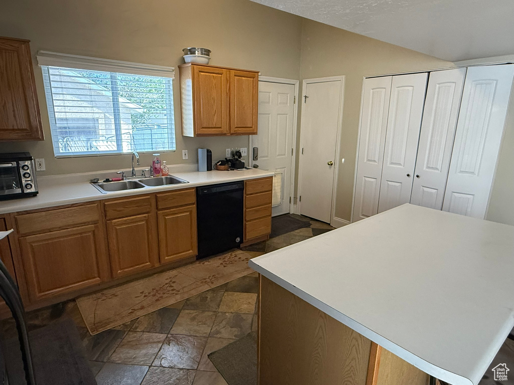 Kitchen with black dishwasher, a sink, vaulted ceiling, light countertops, and dark stone finish floors