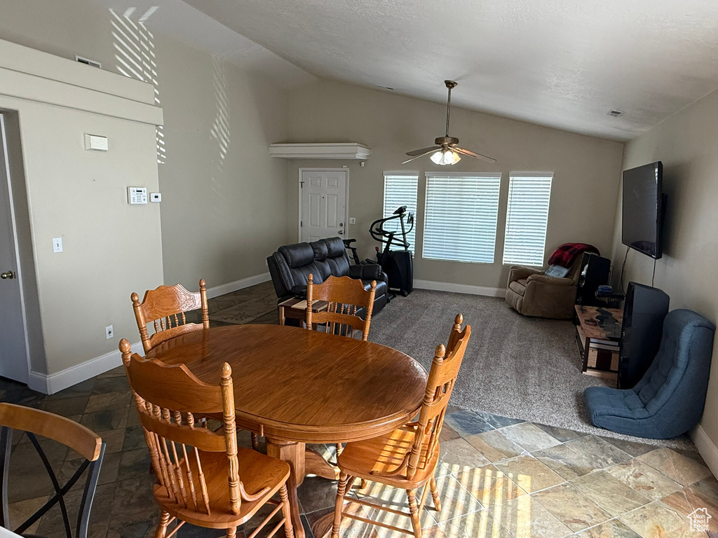 Dining space with lofted ceiling, ceiling fan, light stone finish floors, and baseboards