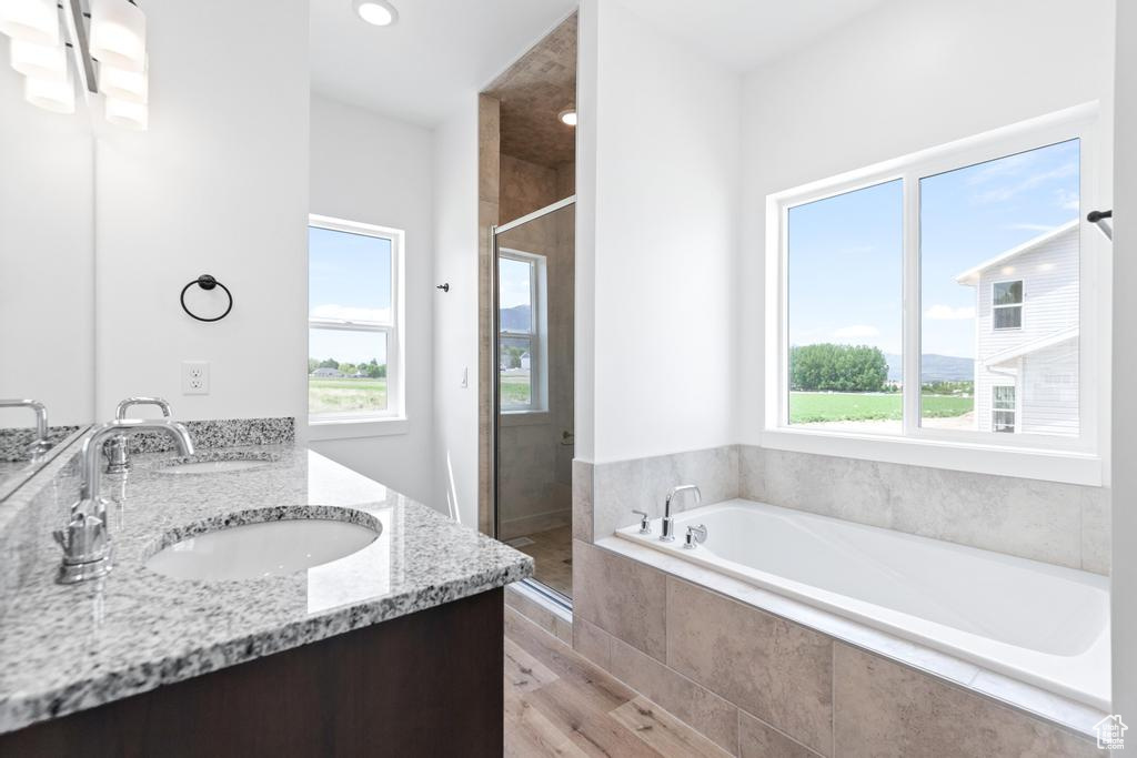 Bathroom featuring a bath, a stall shower, double vanity, and wood finished floors
