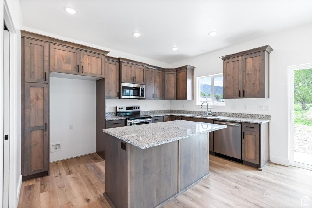 Kitchen featuring appliances with stainless steel finishes, a sink, light wood-style floors, a center island, and light stone countertops
