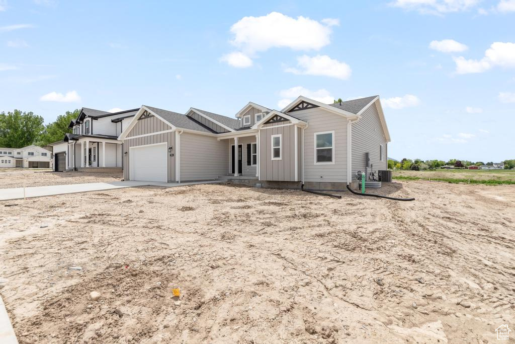 View of front of home with board and batten siding, an attached garage, cooling unit, and driveway