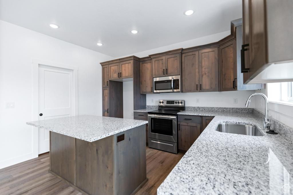 Kitchen with appliances with stainless steel finishes, a sink, dark wood finished floors, a center island, and light stone countertops