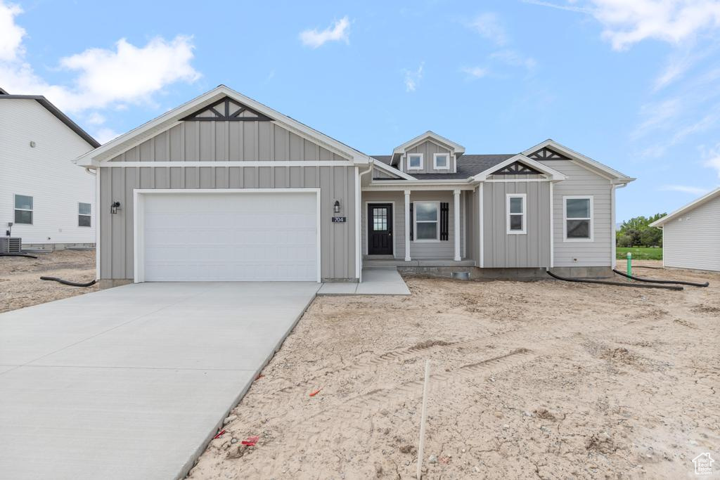 View of front facade featuring an attached garage, board and batten siding, driveway, central AC unit, and covered porch