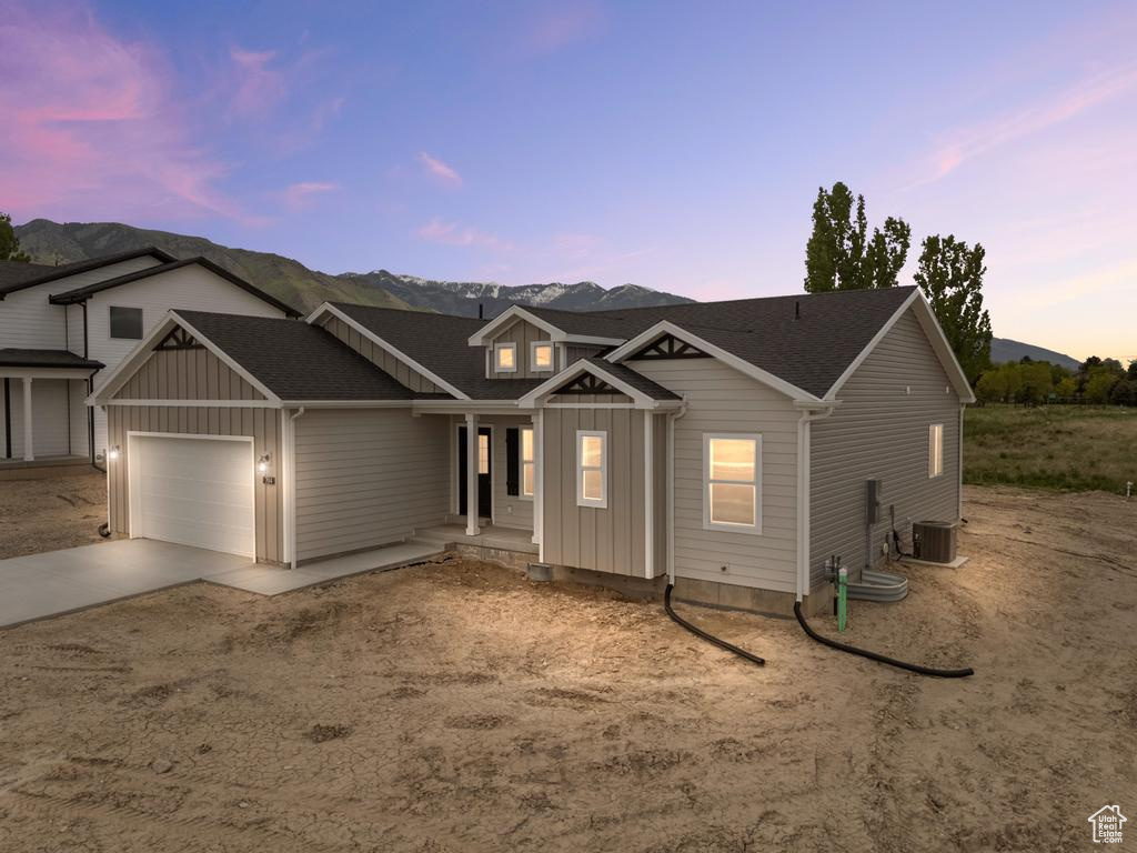 View of front of property with board and batten siding, driveway, an attached garage, a mountain view, and central air condition unit