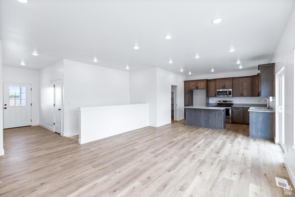 Kitchen featuring stainless steel appliances, open floor plan, a kitchen island, light wood-type flooring, and recessed lighting