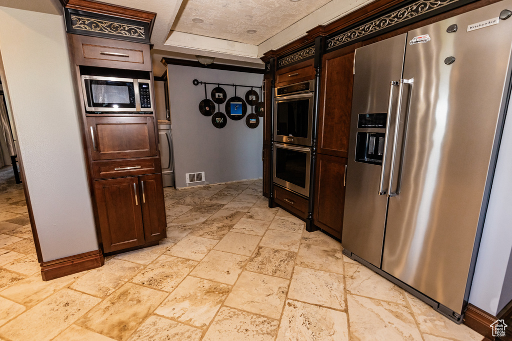 Kitchen featuring appliances with stainless steel finishes, stone tile floors, and dark brown cabinetry