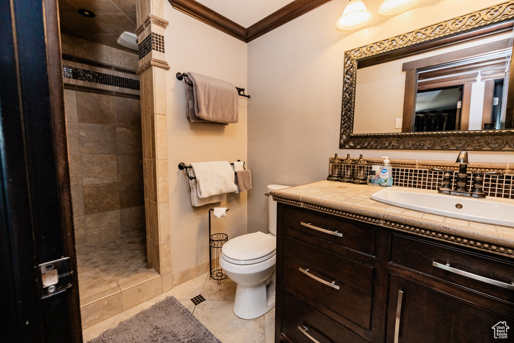 Bathroom featuring crown molding, tiled shower, toilet, vanity, and tile patterned floors