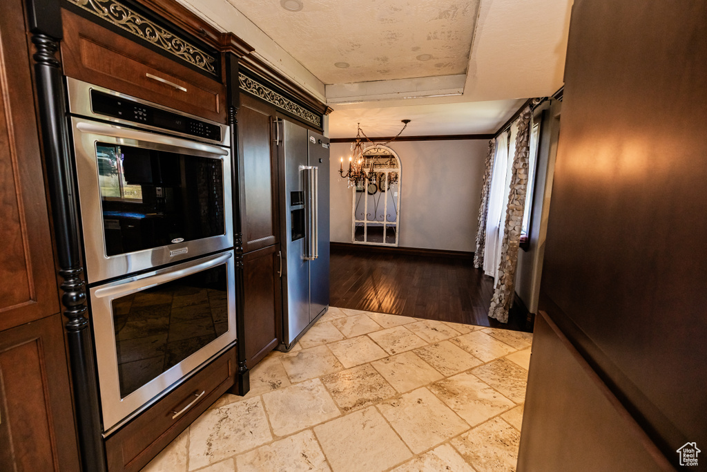 Kitchen with a chandelier, a tray ceiling, stone tile floors, stainless steel double oven, and built in fridge