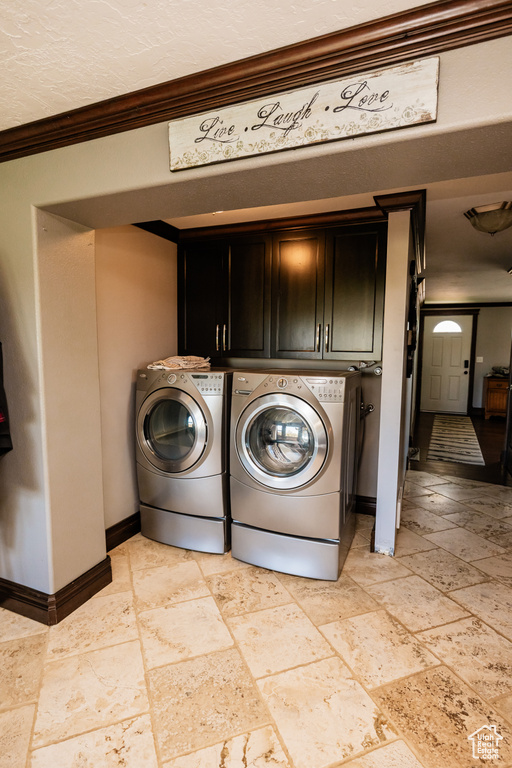 Laundry area featuring cabinet space, crown molding, stone tile floors, baseboards, and separate washer and dryer