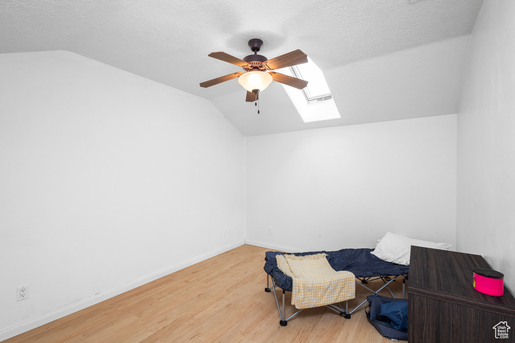 Living area with lofted ceiling, a ceiling fan, wood finished floors, a skylight, and a textured ceiling