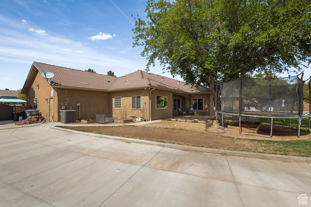 Rear view of house with a trampoline, a tiled roof, stucco siding, and central AC