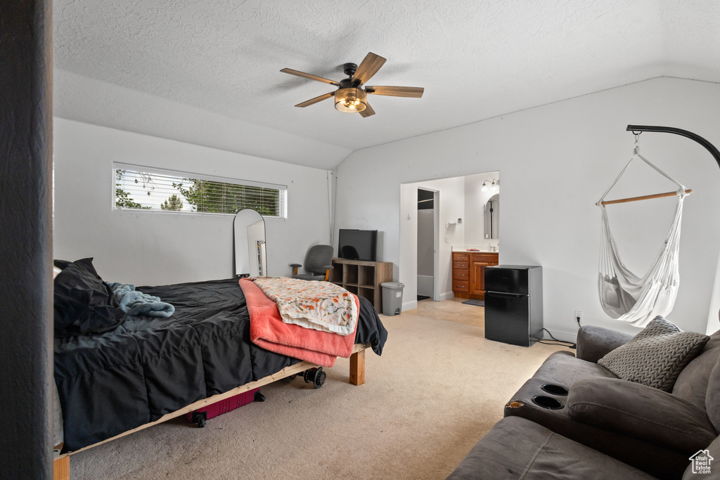 Bedroom featuring vaulted ceiling, light colored carpet, ensuite bathroom, ceiling fan, and a textured ceiling