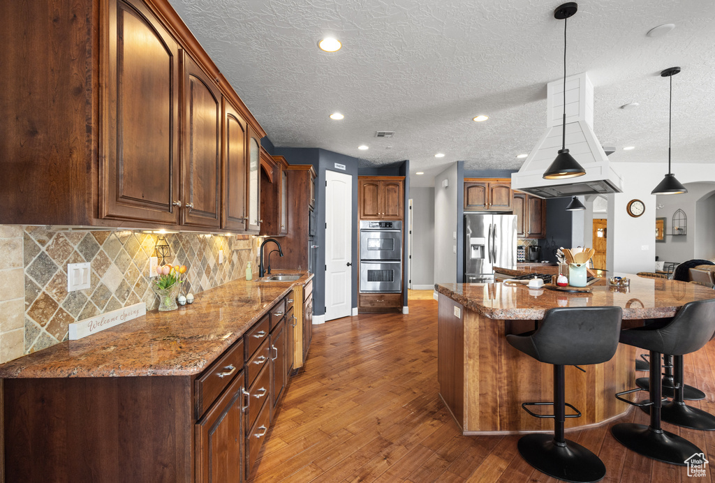 Kitchen with appliances with stainless steel finishes, a sink, dark wood finished floors, a kitchen bar, and decorative backsplash