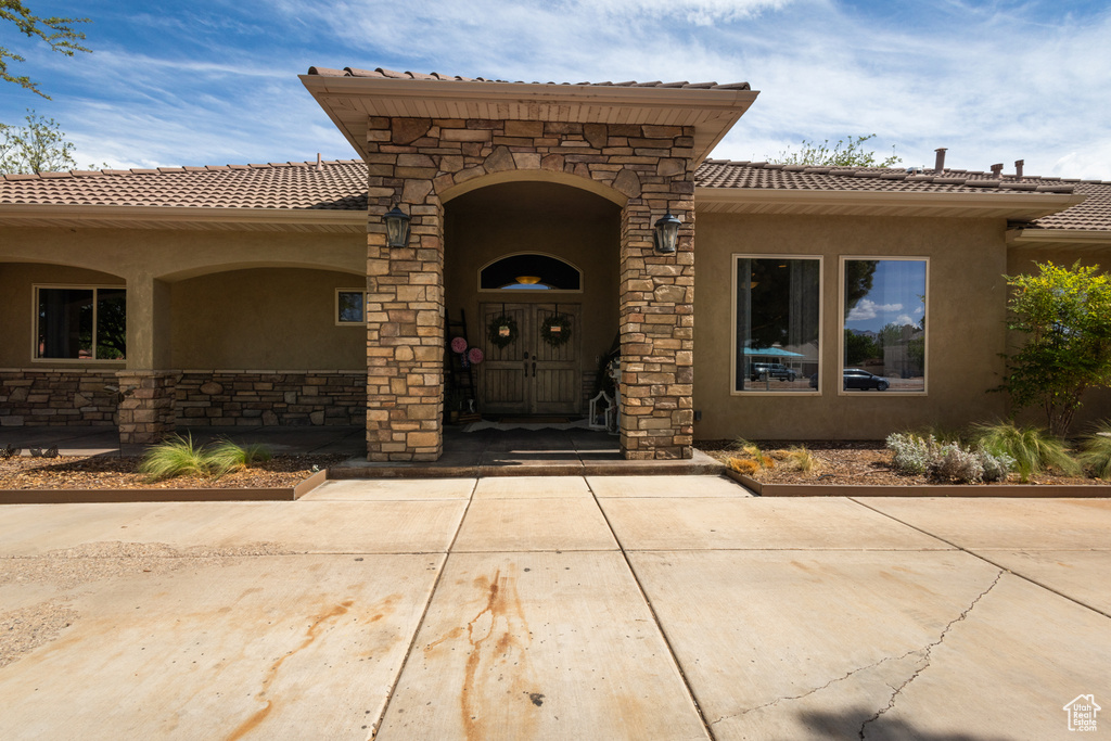 View of exterior entry with stone siding, a tiled roof, and stucco siding