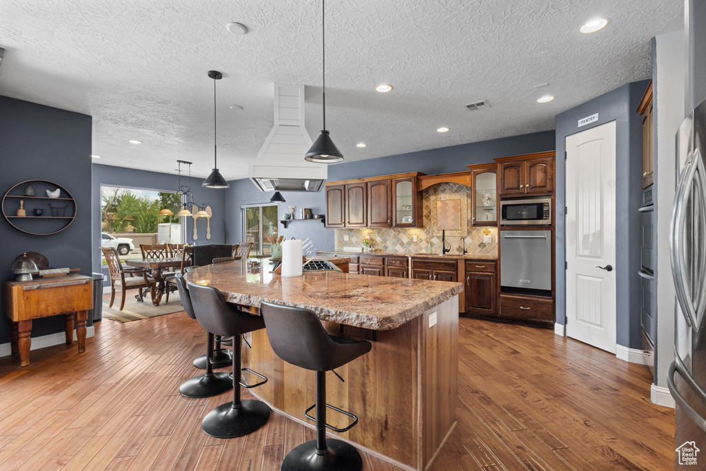 Kitchen featuring stainless steel appliances, a breakfast bar, tasteful backsplash, glass insert cabinets, and light wood-type flooring