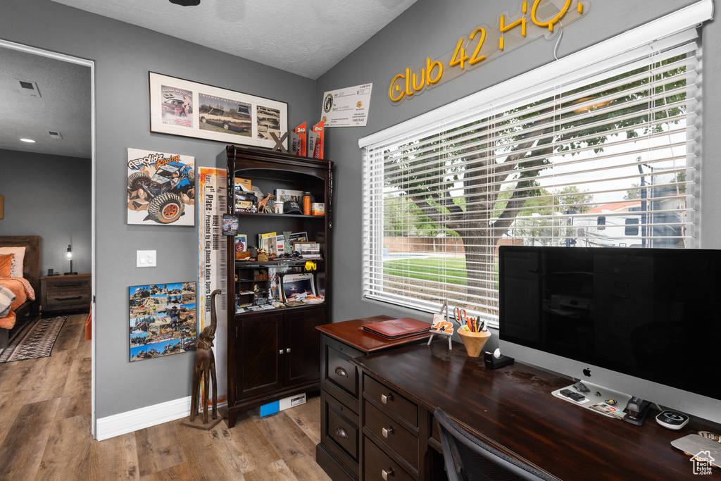 Office area with light wood finished floors, a textured ceiling, and baseboards