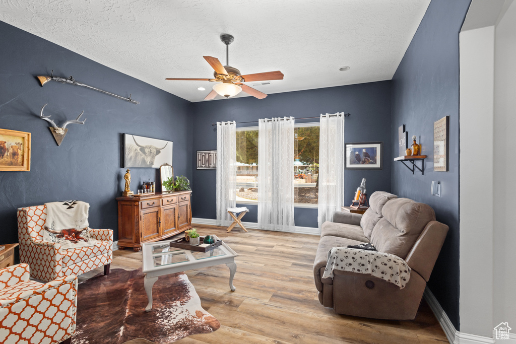 Living area with ceiling fan, light wood finished floors, a textured ceiling, and baseboards