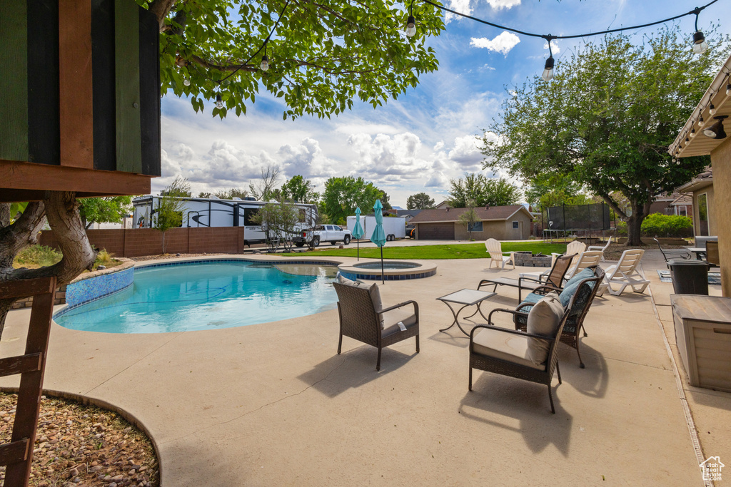 View of swimming pool featuring a patio area, a trampoline, fence, and a pool with connected hot tub