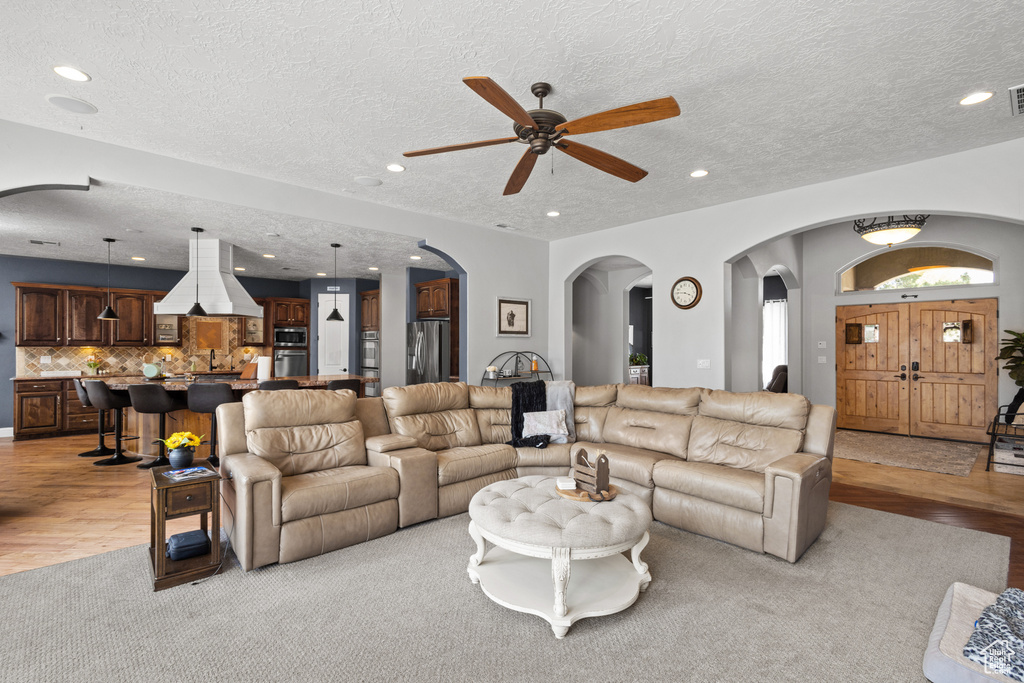 Living area with arched walkways, a ceiling fan, a textured ceiling, light wood-style floors, and recessed lighting