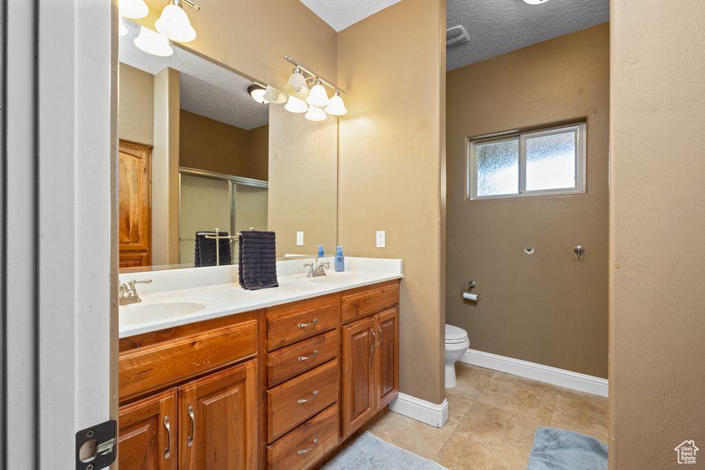 Full bathroom with a shower stall, toilet, double vanity, baseboards, and tile patterned floors