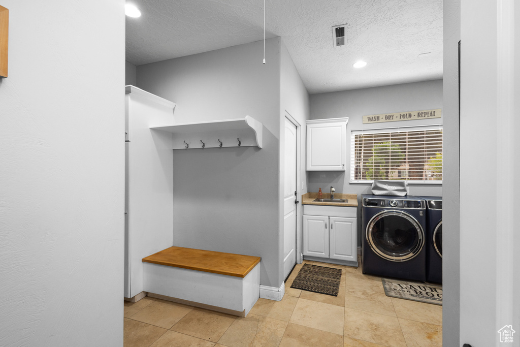 Clothes washing area with cabinet space, washing machine and dryer, a textured ceiling, recessed lighting, and light tile patterned flooring