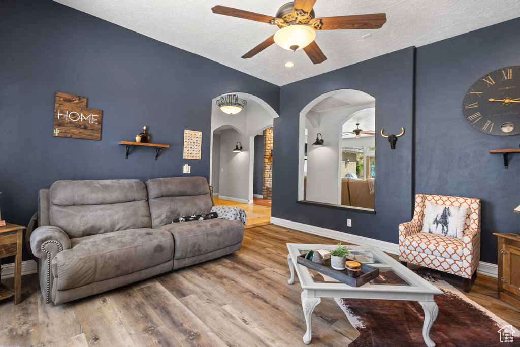 Living room with a ceiling fan, wood finished floors, arched walkways, baseboards, and a textured ceiling