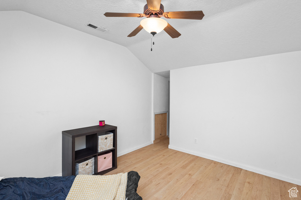 Bedroom featuring lofted ceiling, light wood-style flooring, baseboards, a ceiling fan, and a textured ceiling
