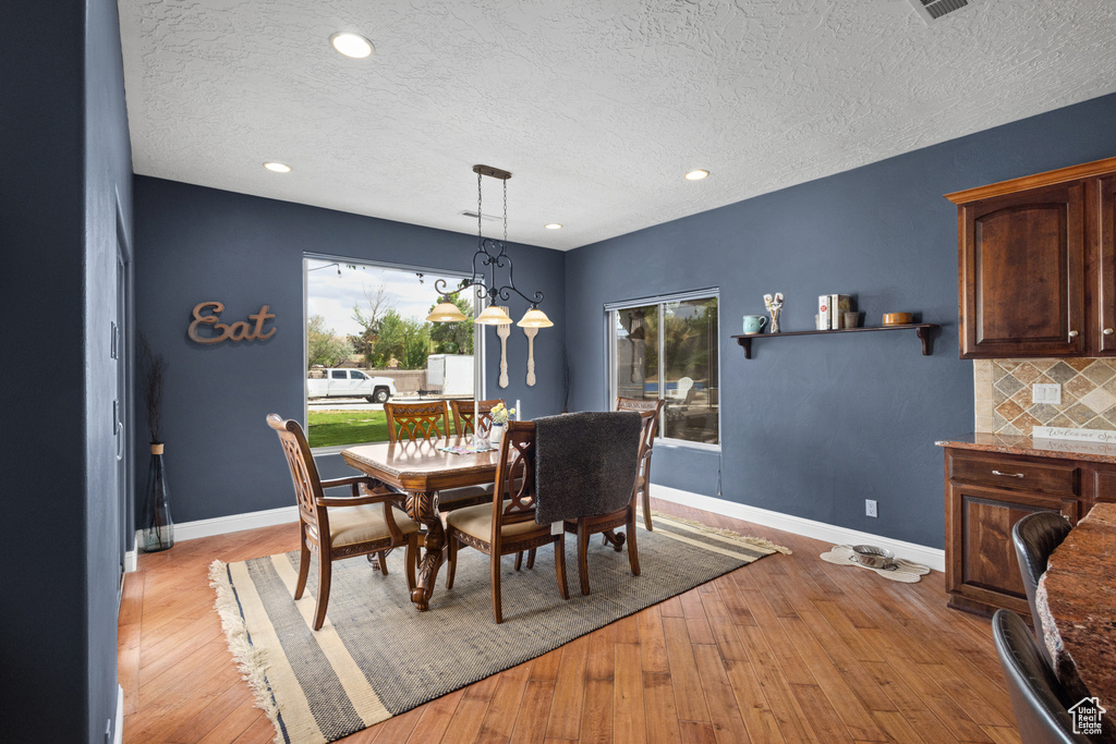 Dining room featuring a textured ceiling, light wood finished floors, baseboards, recessed lighting, and a chandelier