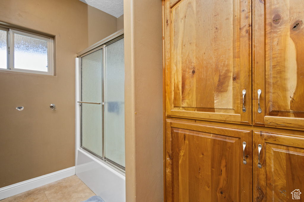 Full bath with baseboards, combined bath / shower with glass door, and tile patterned flooring
