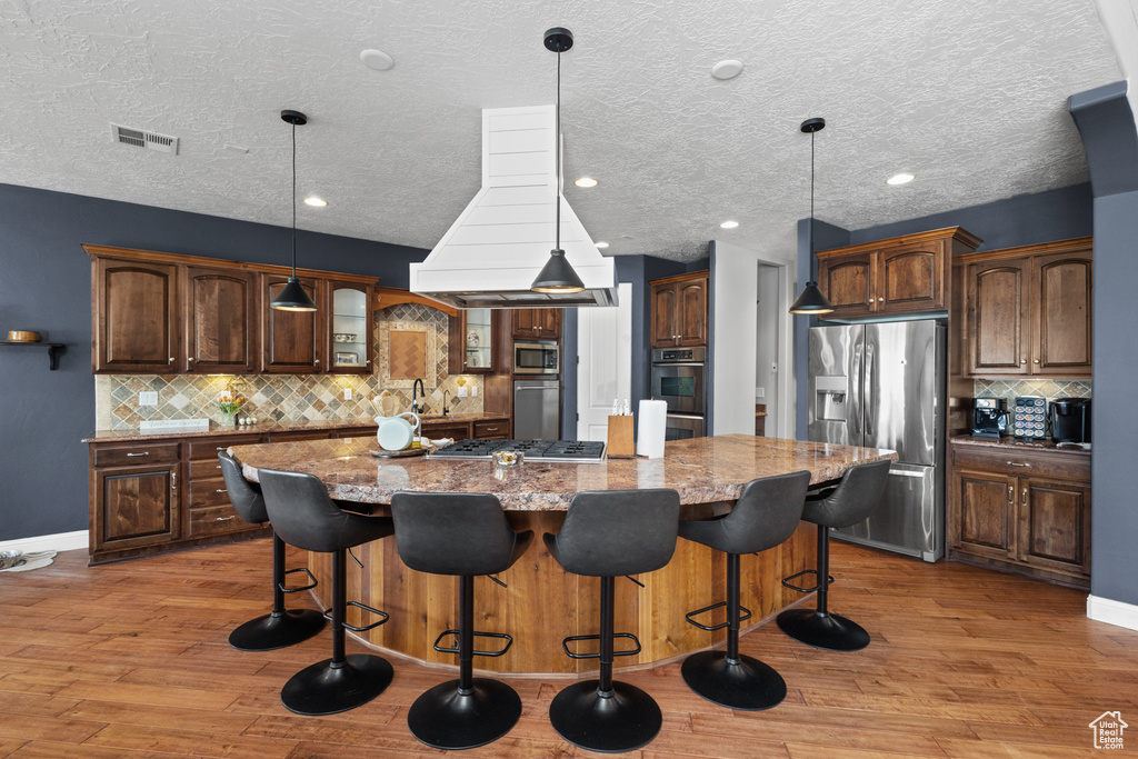 Kitchen with stainless steel appliances, decorative backsplash, light wood finished floors, light stone countertops, and a large island