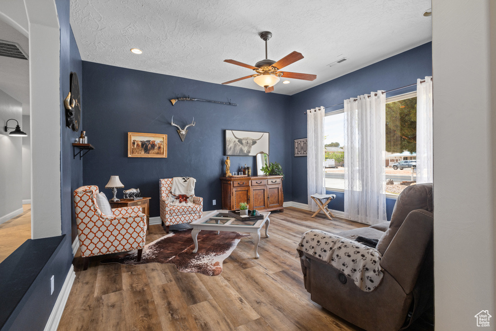 Living room featuring a textured ceiling, ceiling fan, wood finished floors, and baseboards