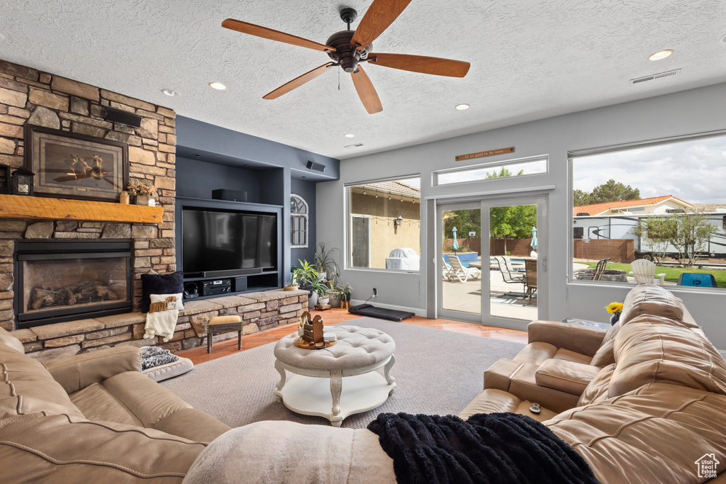 Living area with a textured ceiling, wood finished floors, a stone fireplace, a ceiling fan, and recessed lighting