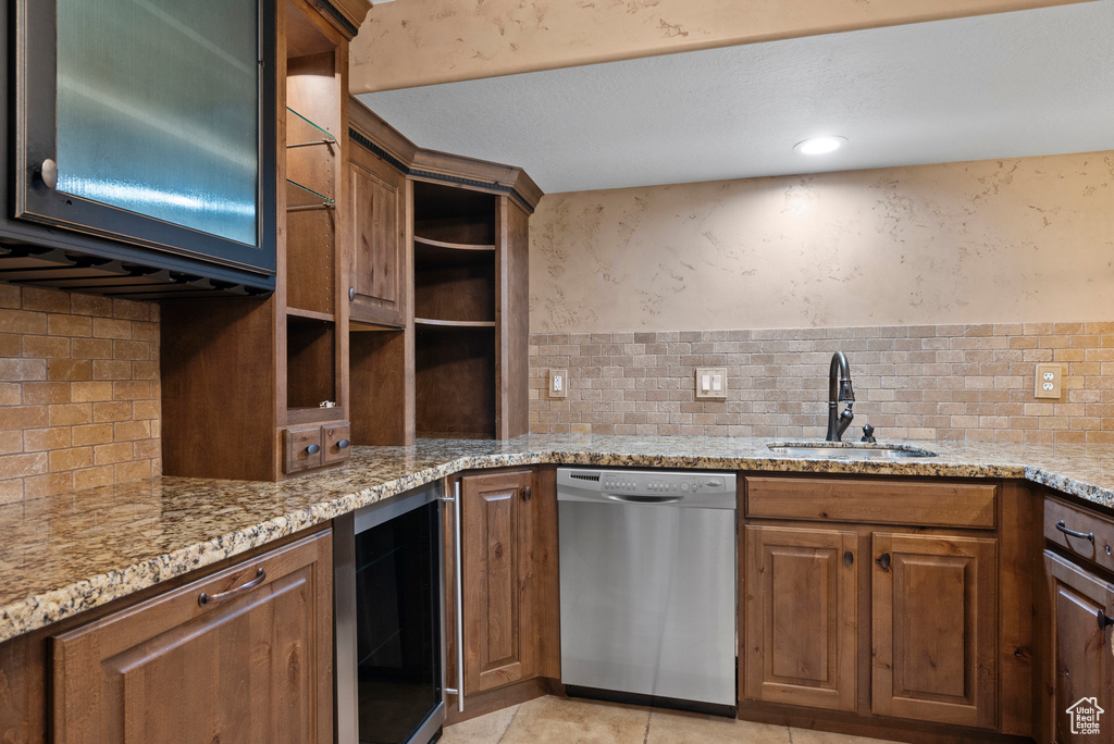 Kitchen featuring a sink, dishwasher, beverage cooler, backsplash, and light stone counters