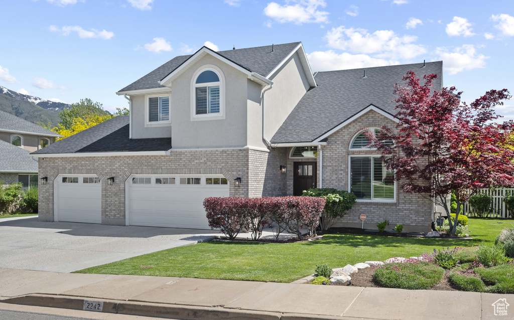 Traditional home with driveway, a front yard, roof with shingles, and brick siding
