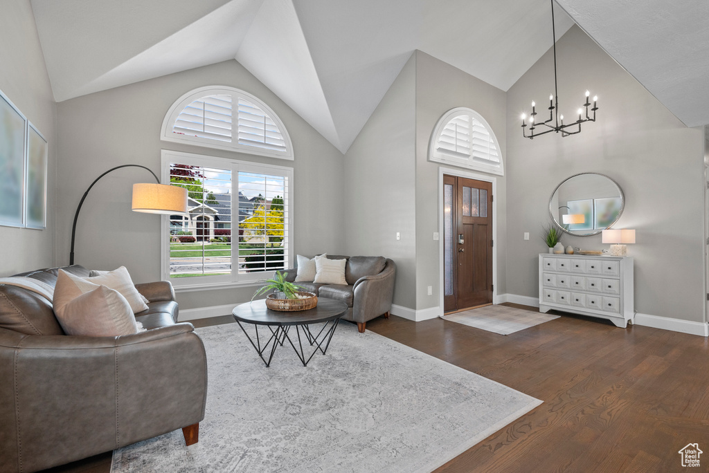 Living room featuring a chandelier, dark wood-type flooring, baseboards, and high vaulted ceiling