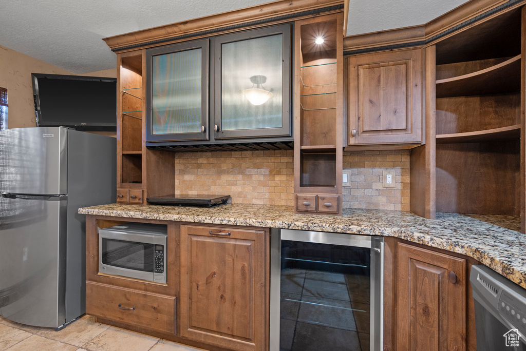Kitchen with beverage cooler, appliances with stainless steel finishes, open shelves, tasteful backsplash, and glass insert cabinets