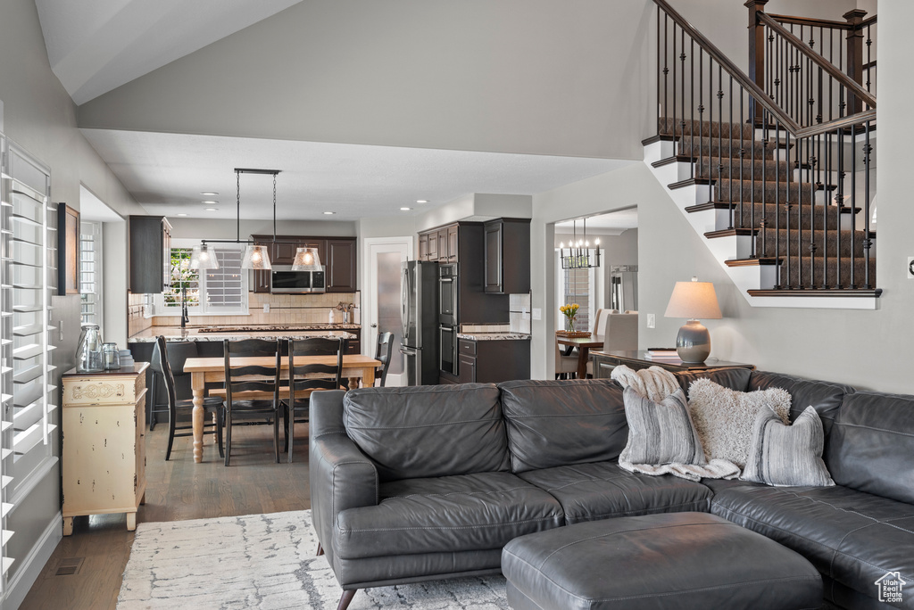 Living room with dark wood-type flooring, high vaulted ceiling, a chandelier, stairway, and recessed lighting