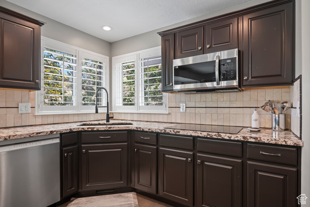 Kitchen with appliances with stainless steel finishes, a sink, light stone countertops, and decorative backsplash